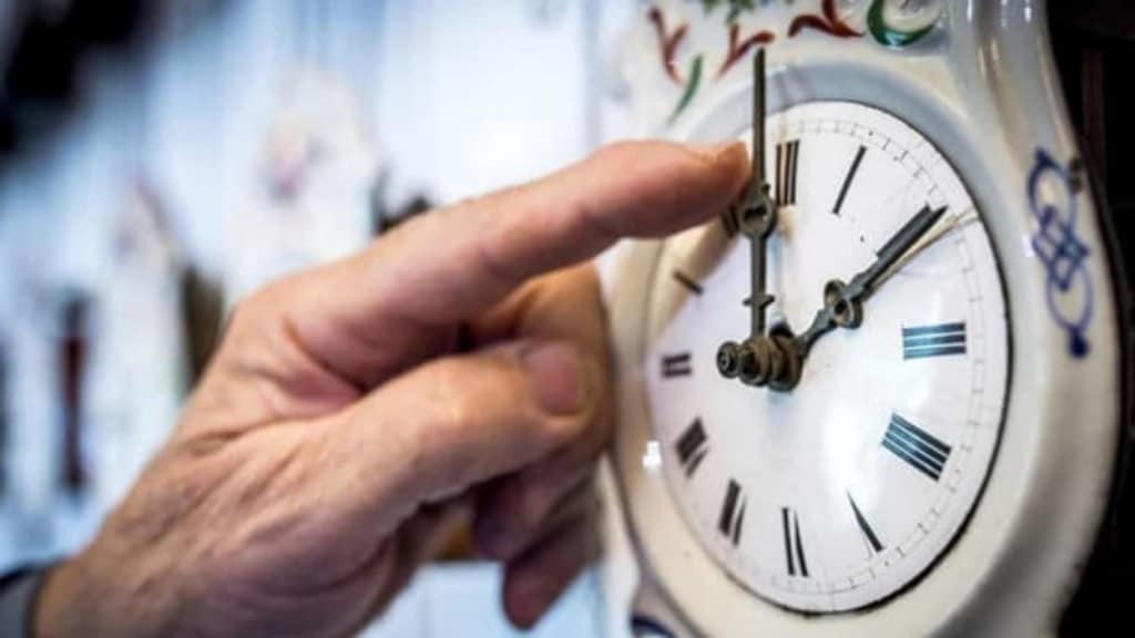 un dito di una persona anziana mentre sposta le lancette su un orologio