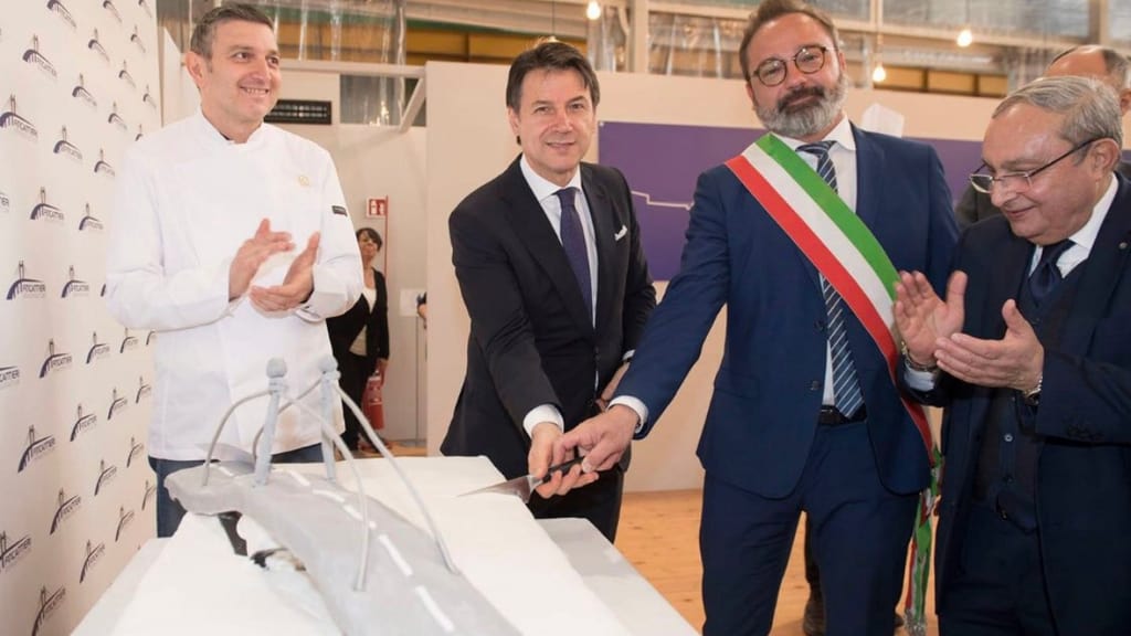 Il primo ministro Giuseppe Conte taglia la torta a forma di ponte per l'inaugurazione dei lavori nello stabilimento Fincantieri