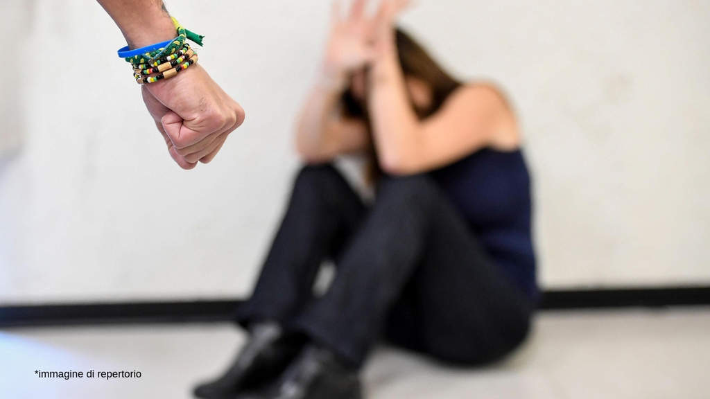 pugno di una persona e di fronte una ragazza che cerca di proteggersi seduta per terra