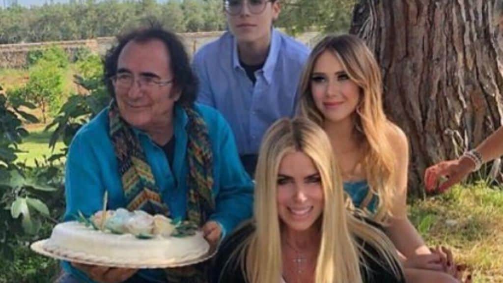 al bano carrisi mentre festeggia con una torta in mano il suo compleanno con affianco i due figli e seduta in basso loredana lecciso