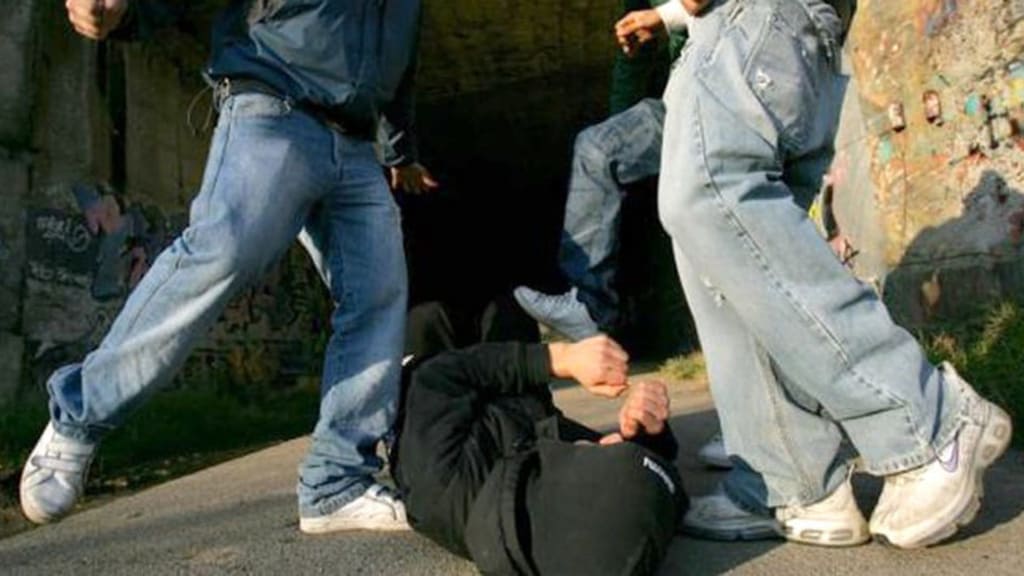 le gambe di 3 ragazzi mentre prendono a calci un ragazzo a terra