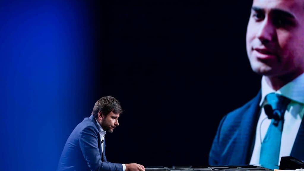 alessandro di battista in studio con alle spalle una foto di di maio