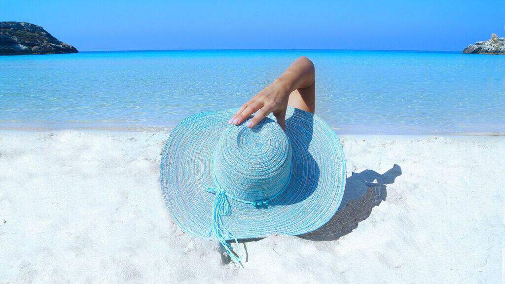 donna sdraiata al mare di spalle con un cappello azzurro