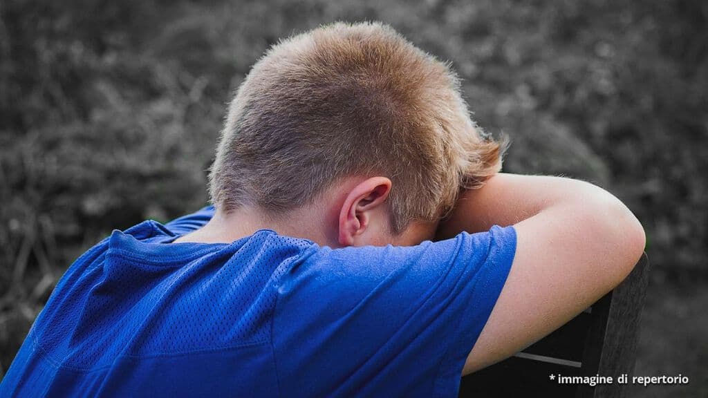 ragazzino che piange seduto su una sedia di spalle