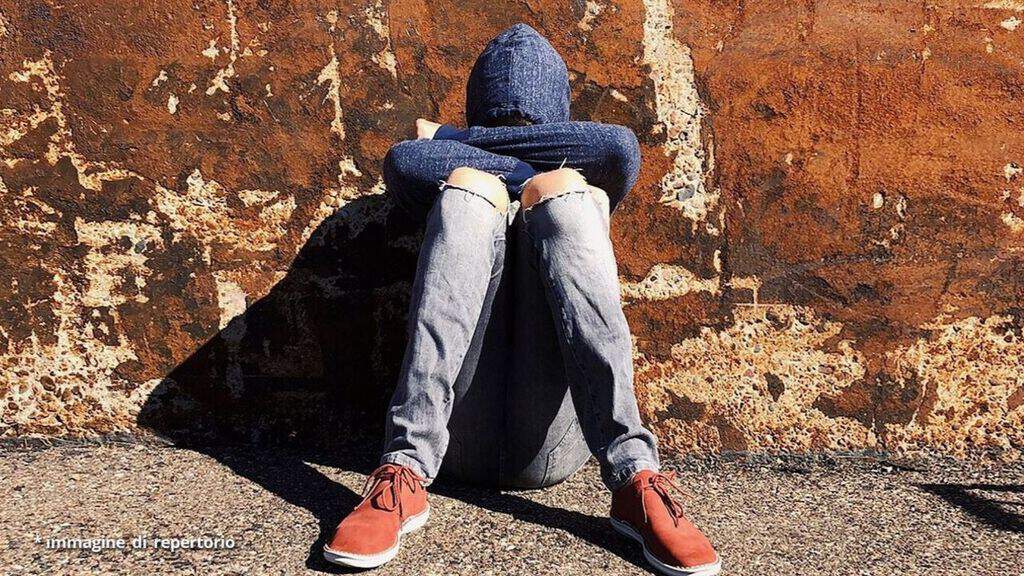 ragazzo in lacrime seduto a terra con il volto coperto