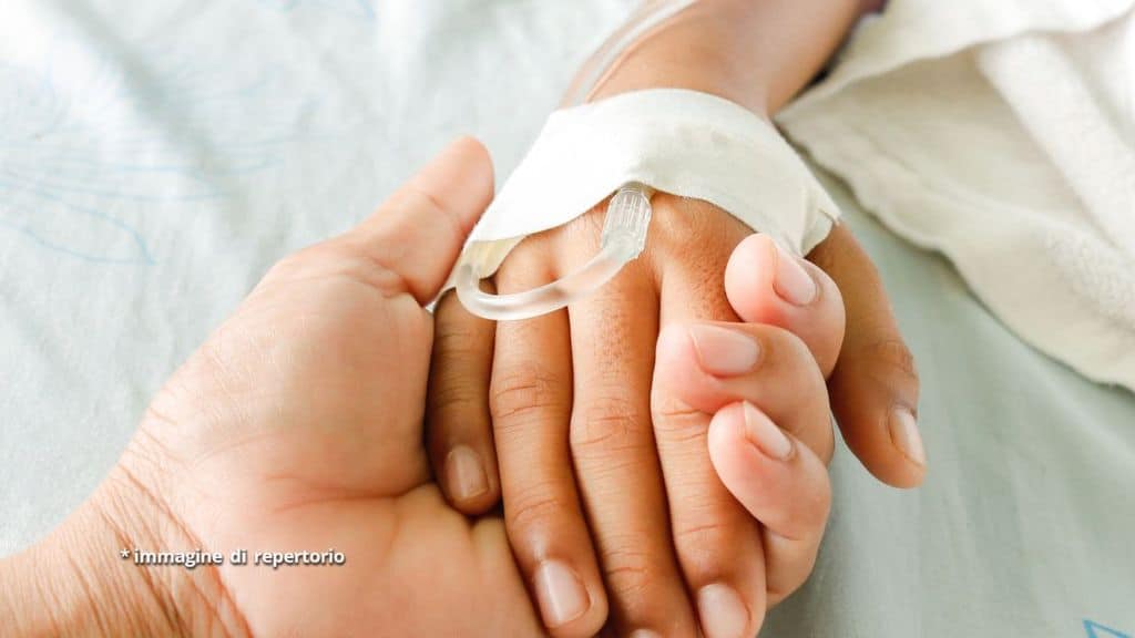 Mano di bimbo con flebo su letto d'ospedale