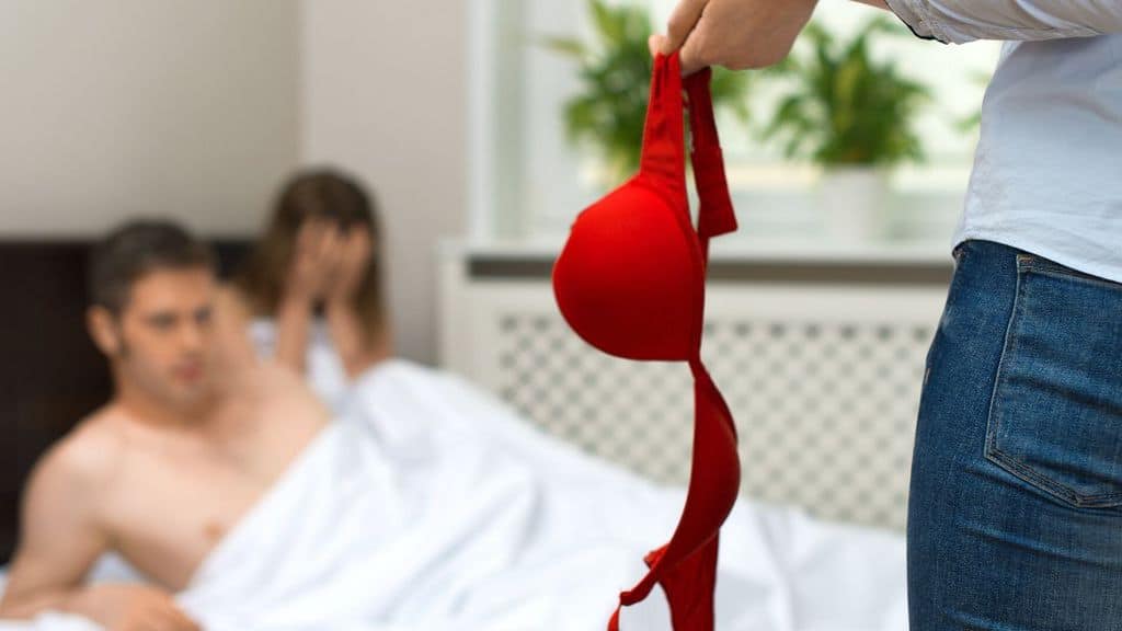 donna che regge un reggiseno mentre scopre il compagno a letto con un'altra