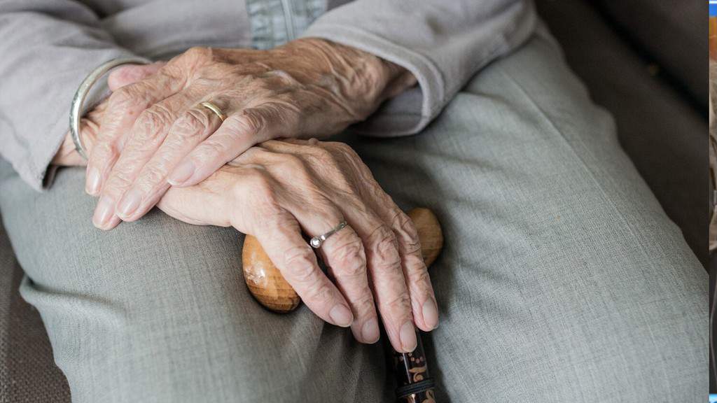 mani di donna anziana appoggiate sulle gambe con un pantalone grigio