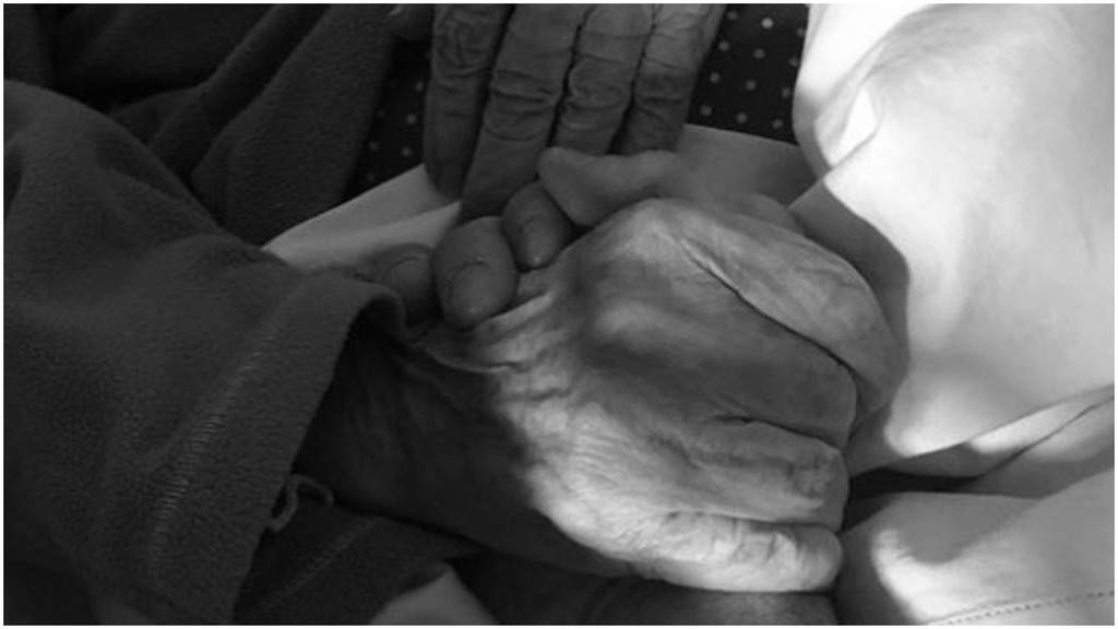 La mano di Luca Vismara tiene stretta quella della nonna sul letto in una immagine in bianco e nero