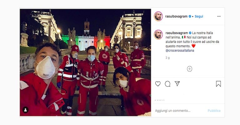 Foto di Raoul Bova e Rocio Monuz Morales insieme a dei volontari della Croce Rossa sulle scale del Campidoglio di Roma, con lo sfondo illuminato con i colori della bandiera dell'Italia