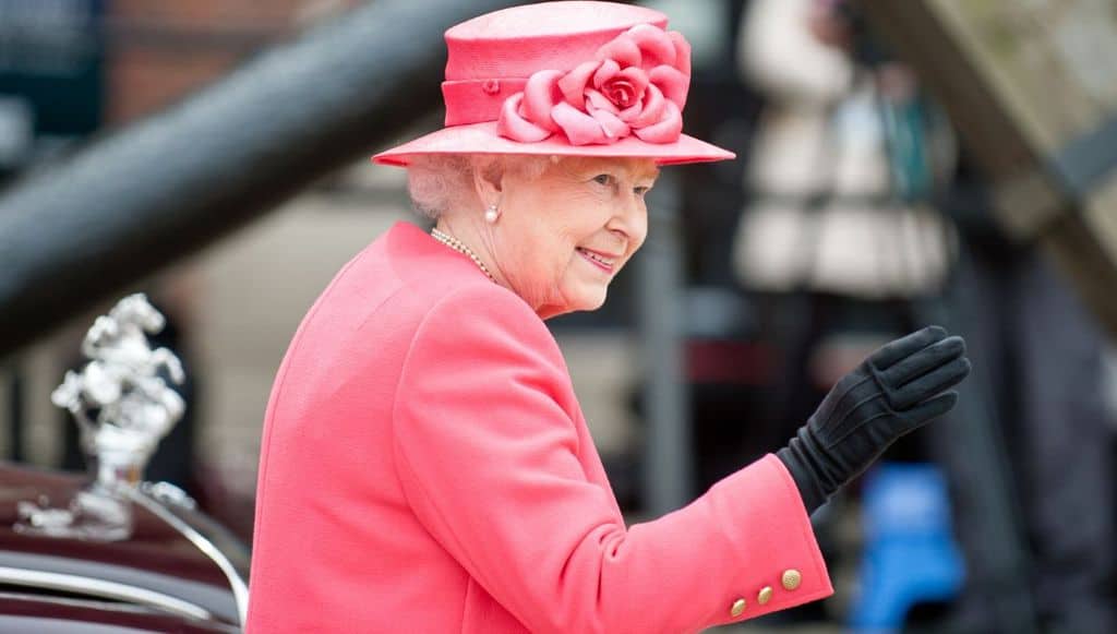 La regina Elisabetta vestita di rosa e sorridente che saluta i sudditi