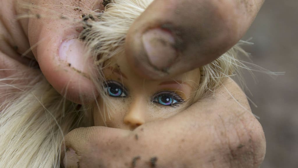 Volto di una barbie stretto tra le mani di un maltrattore