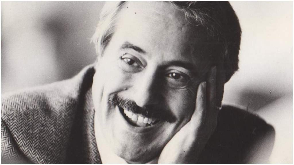 Giovanni Falcone sorridente con il volto appoggiato su una mano