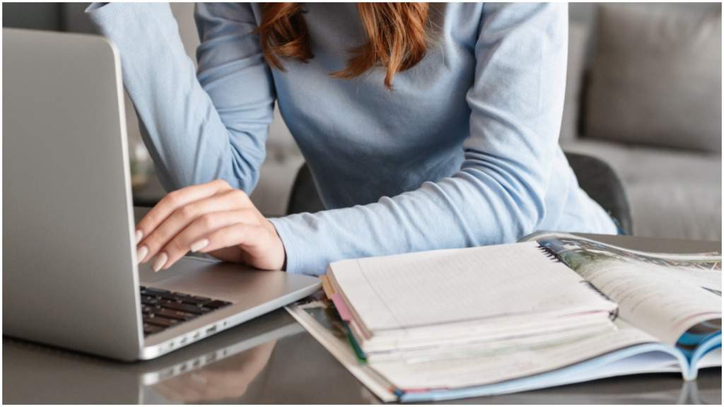 mano di donna sulla tastiera di un pc e dei libri aperti sul tavolo
