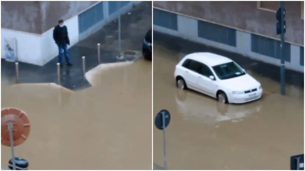una persona su un marciapiede accerchiata dall'acqua in strada e una macchina con l'acqua altezza gomme