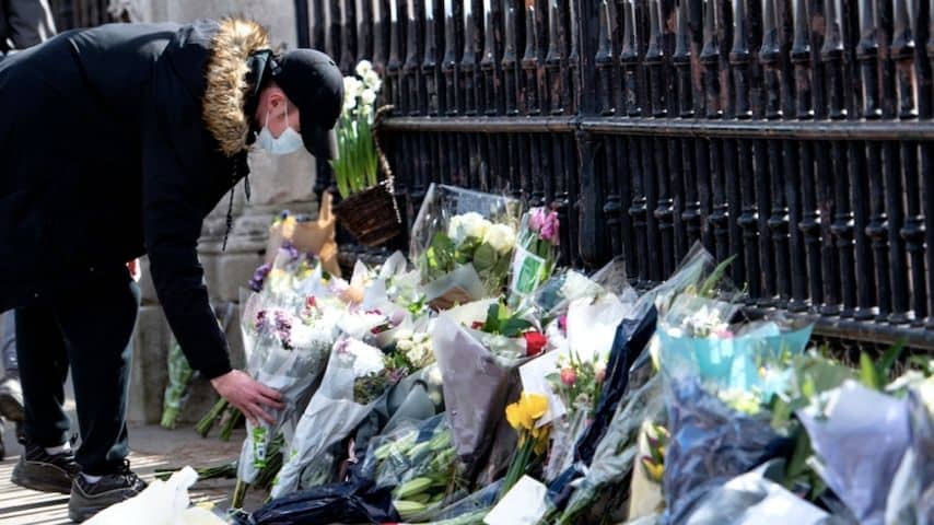 Un uomo pone dei fiori davanti alla cancellata di Buckingham Palace in omaggio al Principe Filppo